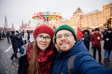 Friends make winter silfie photo woman and man background red square. Concept travel Christmas...