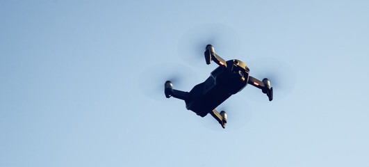 A black copter is flying against a blue sky background. Flying a drone in the sky. Shooting with a camera from the air.