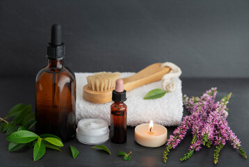 Fototapeta na wymiar Beauty still life with oils, cream, wooden brush, towel, candles, plants and flowers on a gray background. Spa, relaxation and skin care concept.