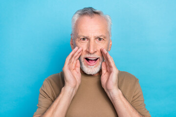 Portrait of positive serious retired man gray hair beard dressed beige t-shirt palms on cheeks shout isolated on blue color background