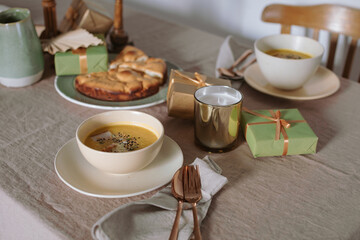 Pumpkin soup, apple pie, candles, gifts on linen tablecloth. Cozy home atmosphere. Family dinner.