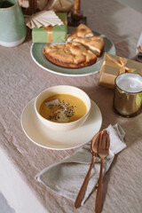 Festive table setting for a family dinner. Pumpkin soup, apple pie, candles, gifts, linen tablecloth. Cozy home atmosphere.