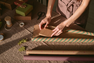 Hands of a woman making a Christmas present. Stylish minimalistic gift packaging. Winter holidays, event celebration. Christmas tradition. 