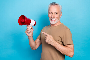 Portrait of optimistic funny retired man gray hair beard dressed beige t-shirt directing at megaphone isolated on blue color background