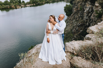Fototapeta na wymiar A stylish groom and a beautiful, sweet bride in a white dress are embracing in the open air, against the backdrop of rocks, mountain cliffs near the sea. Wedding photography, portrait.