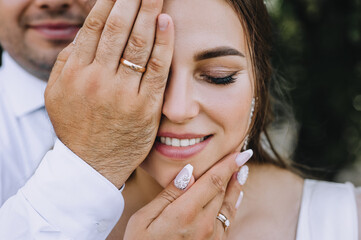 The groom covers half of the bride's face with his hand. Close-up wedding photography, portrait,...