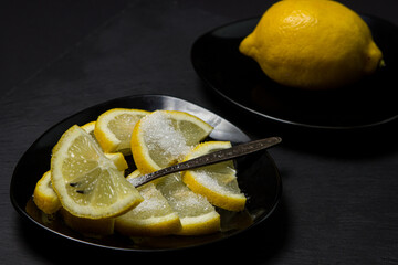 Lemon slices in sugar on a black background. Sliced lemon on a black plate
