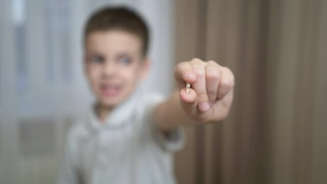 The boy shows his first lost milk tooth. First grader holding a milk tooth in his hand