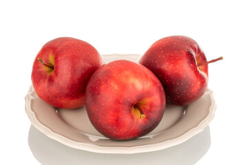 Three red apples on a white ceramic plate, macro, isolated on a white background.