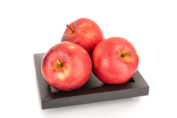 Still life of three red apples on a black wooden plate, macro, isolated on white background.