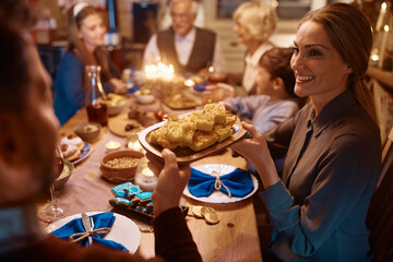 Happy woman passing food to her husband during family dinner on Hanukkah.