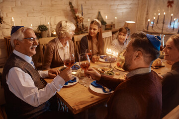 Happy Jewish men toasting with wine during family dinner on Hanukkah.