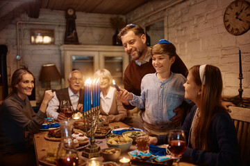 Happy father and son lighting candles in menorah during family dinner on Hanukkah.