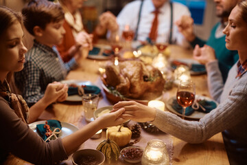 Close up of extended family saying grace during Thanksgiving dinner at dining table.