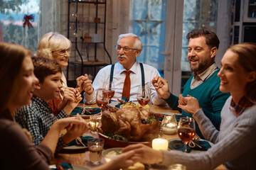 Happy multigeneration family holding hands and talking after the saying grace during Thanksgiving dinner at dining table.