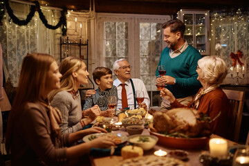 Happy father holding toast while celebrating Thanksgiving with his extended family at dining table.
