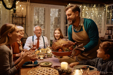 Happy father serving Thanksgiving turkey to his extended family at dining table.