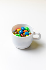 Taza blanco con bolas de chocolate de colores con fondo blanco y mano cogiendo golosinas