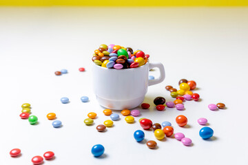 Taza blanco con bolas de chocolate de colores con fondo blanco y amarillo y mano cogiendo golosinas