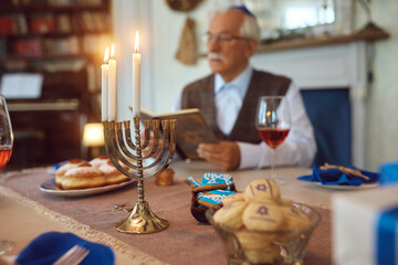 Lit candles in menorah with Jewish senior man in background. - obrazy, fototapety, plakaty