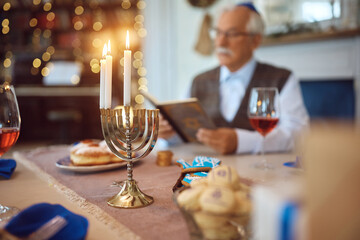 Close up of menorah with senior man reading Tanakh during Hanukkah.