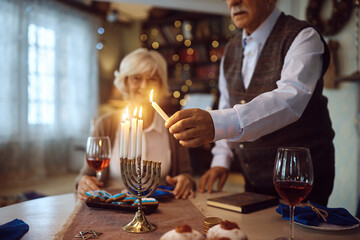 Close up of senior man lighting menorah while celebrating Hanukkah with wife at home.