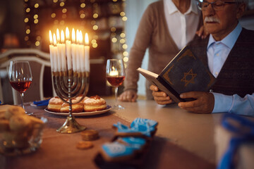 Close up of senior couple reading Tanakh while celebrating Hanukkah at home. - obrazy, fototapety, plakaty