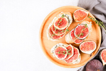 Fresh bruschettas with raw fig, cheese, prosciutto and herbs wooden plate with copy space on white background. Healthy on-the-go breakfast recipe. Top view, selective focus