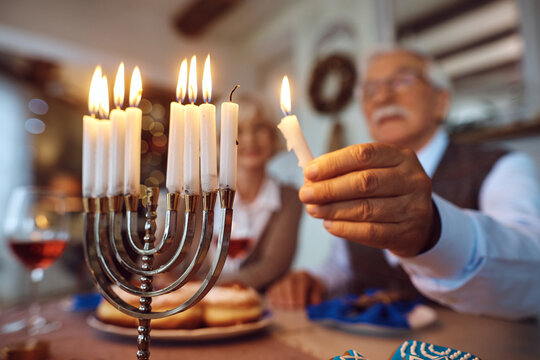 Close up of senior Jewish man lighting candle in menorah while celebrating Hanukkah with his wife.