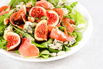 Healthy food recipe - salad with fresh fig, blue cheese, prosciutto, arugula and spinach on white table background with copy space. Lunch idea. Selective focus