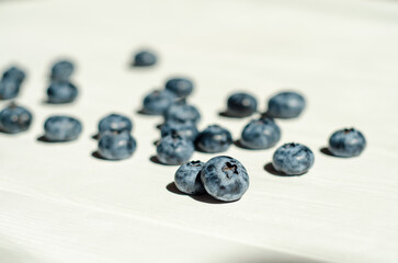 Obraz na płótnie Canvas Fresh blueberry berries lie under the sunlight with shadows on a white wooden background. The topic of ecological, healthy and natural food, vegans. With copyspace
