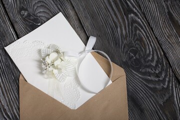 Homemade greeting card in white. With decorative elements. Ribbons, flowers and leaves are attached to cardboard. Paper envelope. Close-up.