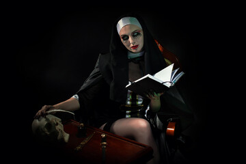 An evil cursed nun with a notebook and a cross in her hands looks at the camera on a black...