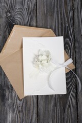 Homemade greeting card in white. With decorative elements. Ribbons, flowers and leaves are attached to cardboard. Paper envelope. Close-up.