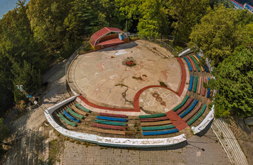 a dance floor with a stage and benches for spectators in an old children's pioneer camp built during the USSR, with symbols of the 1980 Olympics - aerial view from above