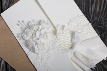 Homemade greeting card in white. With decorative elements. Ribbons, flowers and leaves are attached to cardboard. Paper envelope. Close-up.