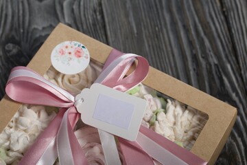 Homemade marshmallows in a gift box. Tied with ribbon. Zephyr flowers. On black pine boards. Taken from above.