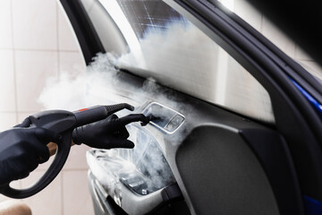 Steam vaping cleaning inside handle of car door after foam washing with brush. Worker in car detailing service washing leather interior of clients auto using steam generator.