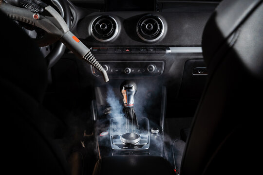 Steam cleaning of gearbox and dashboard in car. Vaping steam. Cleaning individual elements of black leather interior in auto. Creative advert for auto detailing service.