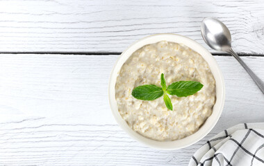 White bowl of oatmeal or oatmeal porridge on a wooden white background. Top view, copy space.
