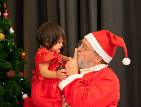 Side View Of Santa Claus Comforts Crying Kid Little Girl At Home.