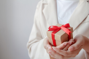 Woman hand holding a small gift wrapped with red ribbon.