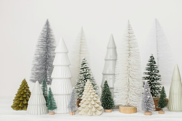 Merry Christmas and Happy Holidays! Stylish little Christmas trees on white background. Festive Christmas scene, miniature snowy forest. Modern minimal scandi decorations, holiday banner