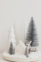 Stylish little Christmas trees and reindeer toy on white table. Festive Christmas scene, miniature...