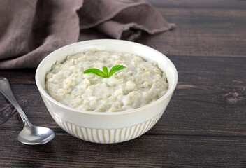 White bowl of oatmeal with milk on a brown wooden background. Side view.