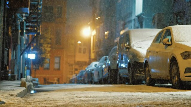 Snow falling at empty backstreet with parked cars, street with no people at night during snowfall. Backyard of big city, snow storm, no people, background