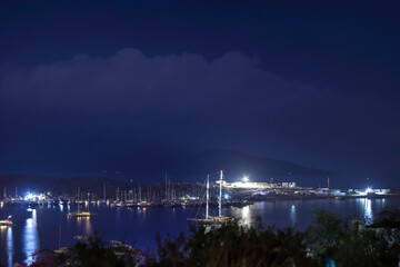 Fototapeta premium Boat on the sea, harbor and lights reflecting on the sea at blue hour on a rainy and cloudy evening.