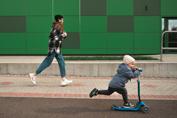 Mother help her son ride with kick scooter. Happy family mother teaches child son to ride a scooter in the Park. Support childhood parenthood idea. happy family concept