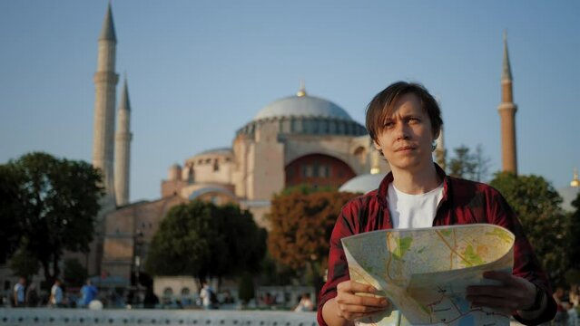 Man tourist looking at paper map against Ayasofya (Hagia Sophia) Mosque, travel Concept. Guy wearing shirt holding and navigating with topographic map by city, popular area in Istanbul Fatih