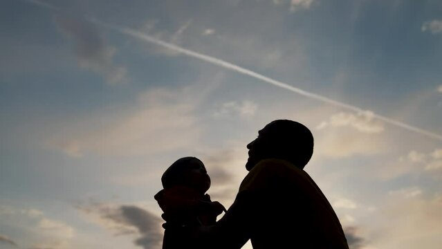 Happy family walks in park outdoors. Silhouette of happy family. Silhouette of father throwing happy child into air at sunset. Silhouette of child against sky in hands of his father.